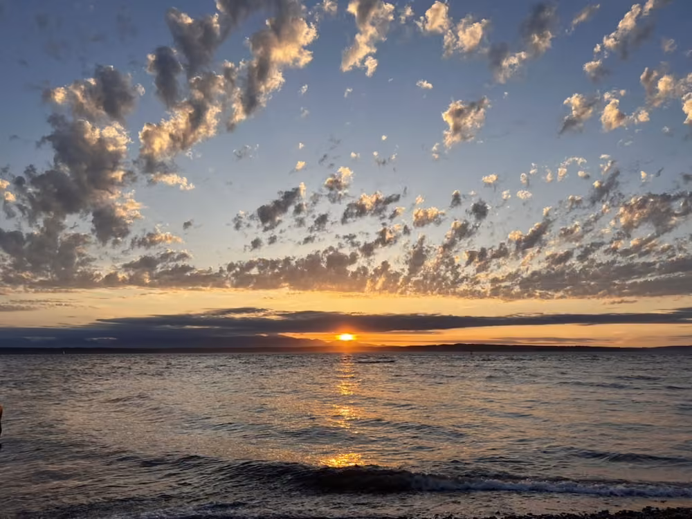 The sun setting over the water under a sky of scattered clouds